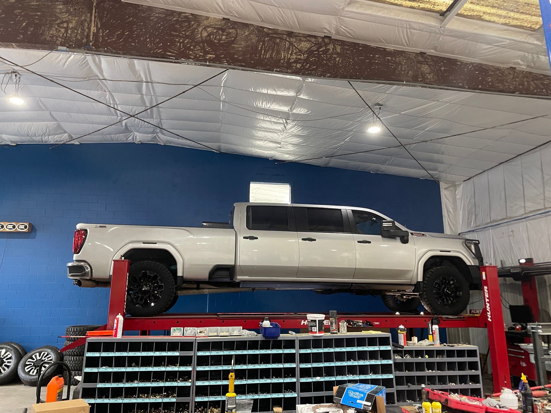 Silver pickup truck on a red lift inside a shop with a blue wall. Black wheels, parts organizer below | Marshside Motors