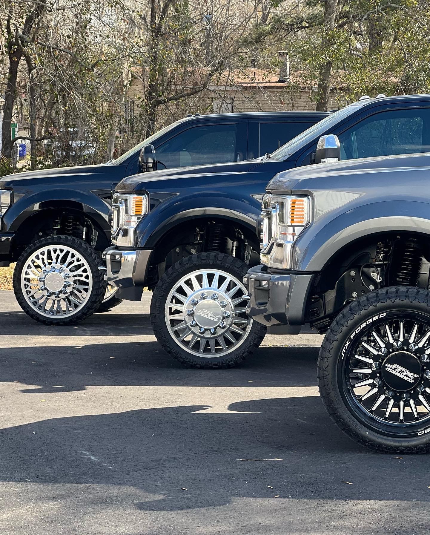 Three lifted, dark-colored pickup trucks parked outdoors with large chrome and black wheels | Marshside Motors