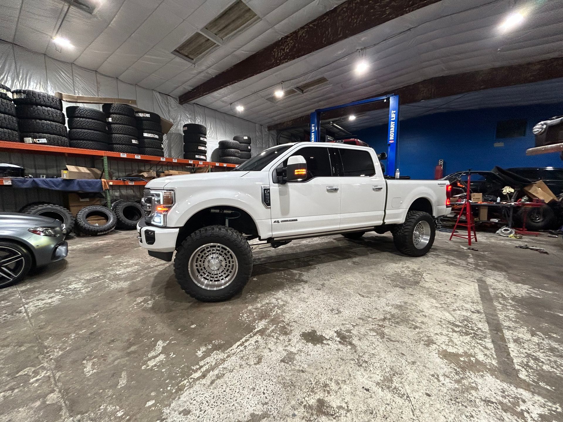 White lifted pickup truck inside a garage with tires and shelves | Marshside Motors