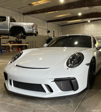 White Porsche 911 GT3 in a garage with a lifted silver pickup truck in the background | Marshside Motors