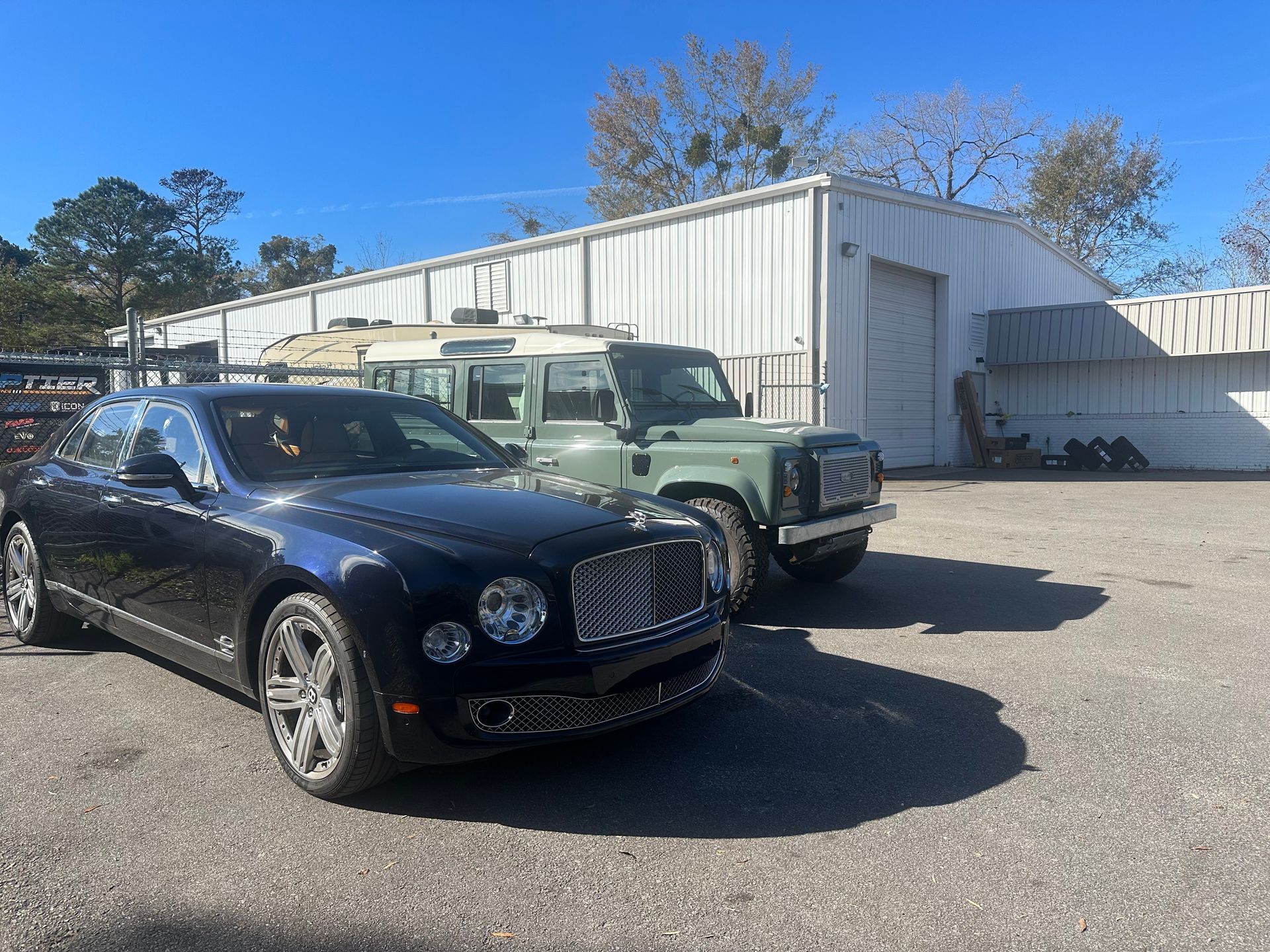 Dark blue Bentley and green Land Rover parked outside a white industrial building on a sunny day | Marshside Motors