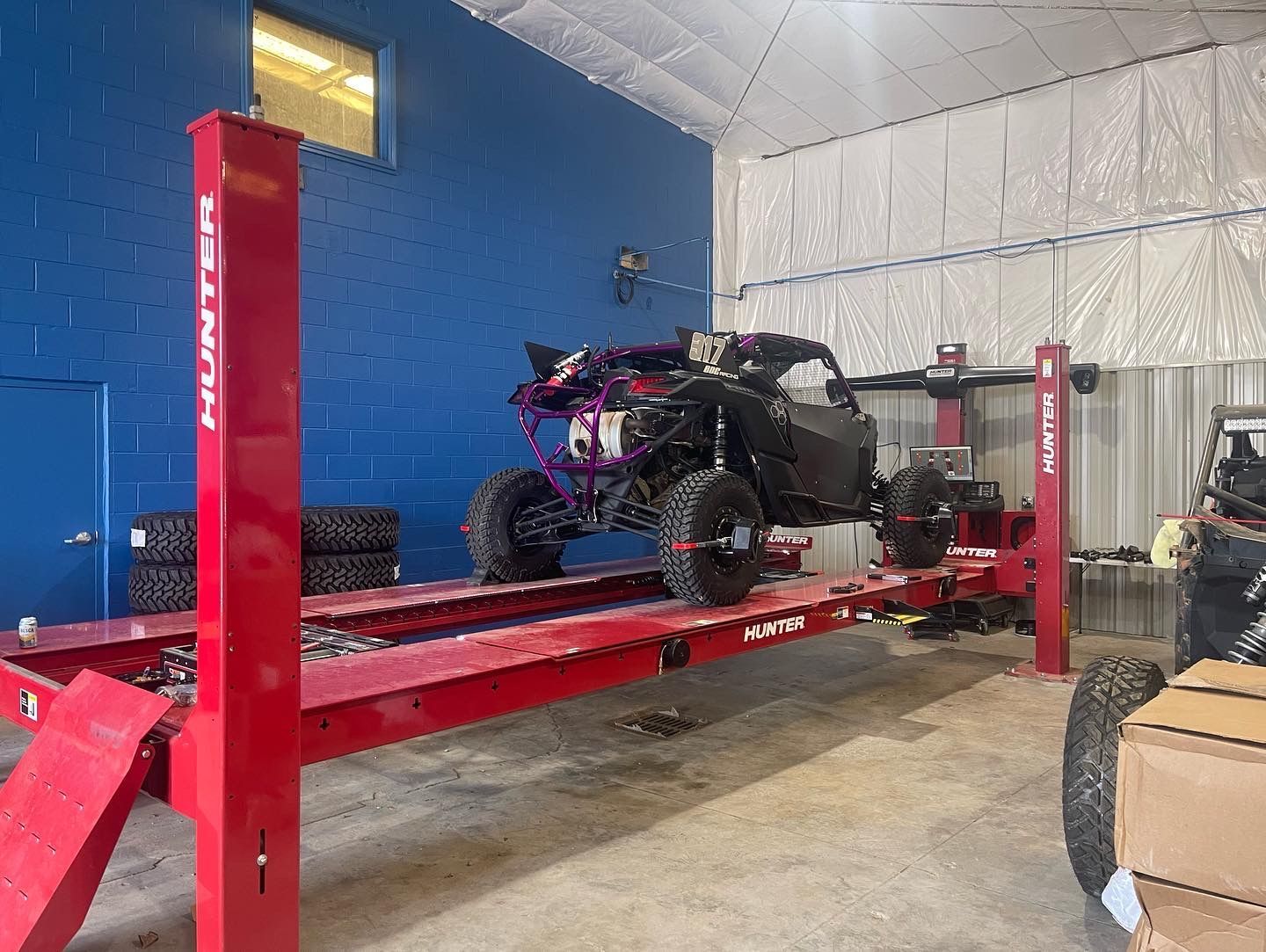 Red car lift holding a black ATV inside a shop with a blue wall | Marshside Motors