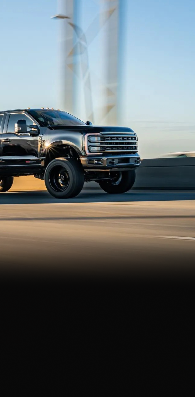 Black truck driving on a bridge, with a blurred background of the sky and structures | Marshside Motors