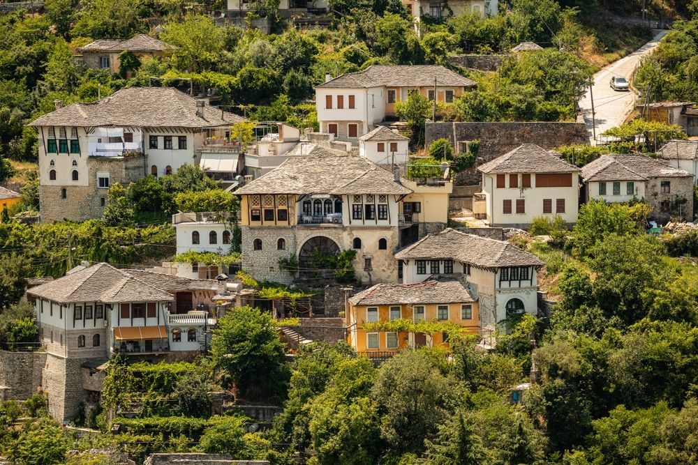 Village in Albania, historic stone houses with tiled roofs, nestled in lush green trees on a hillside.