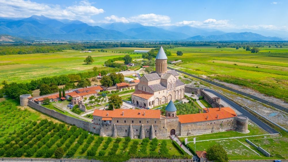 Medieval Gremi church and fortress in Kakheti, Georgia, surrounded by green fields, mountains in the background.