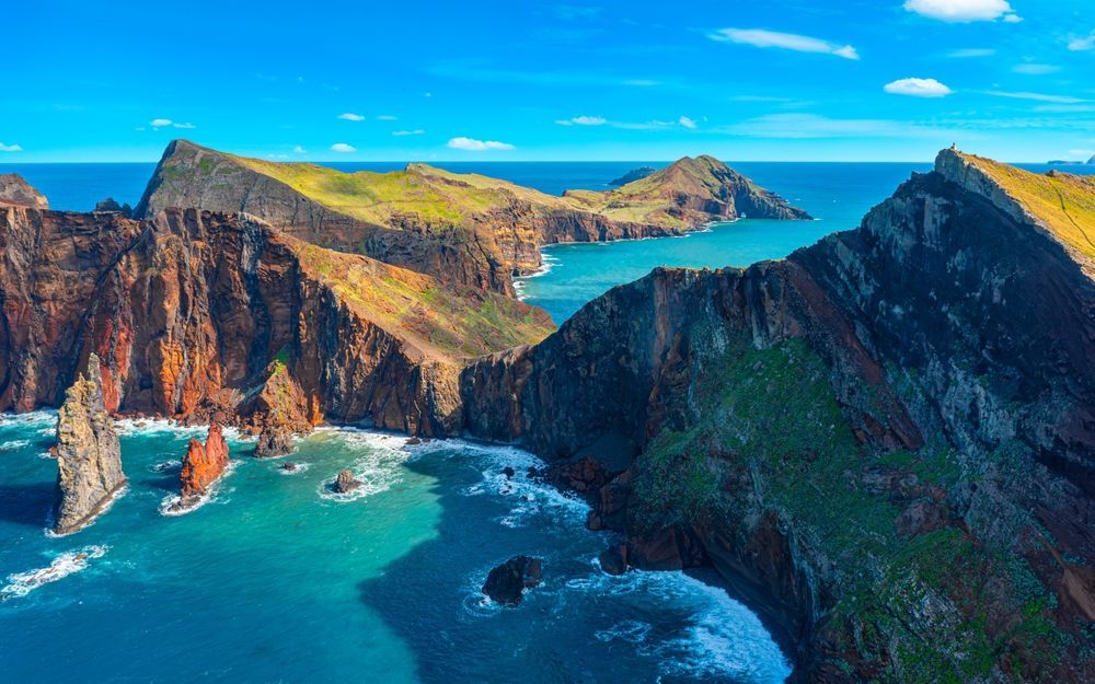Rocky cliffs meet the turquoise ocean under a blue sky, near a coastline.