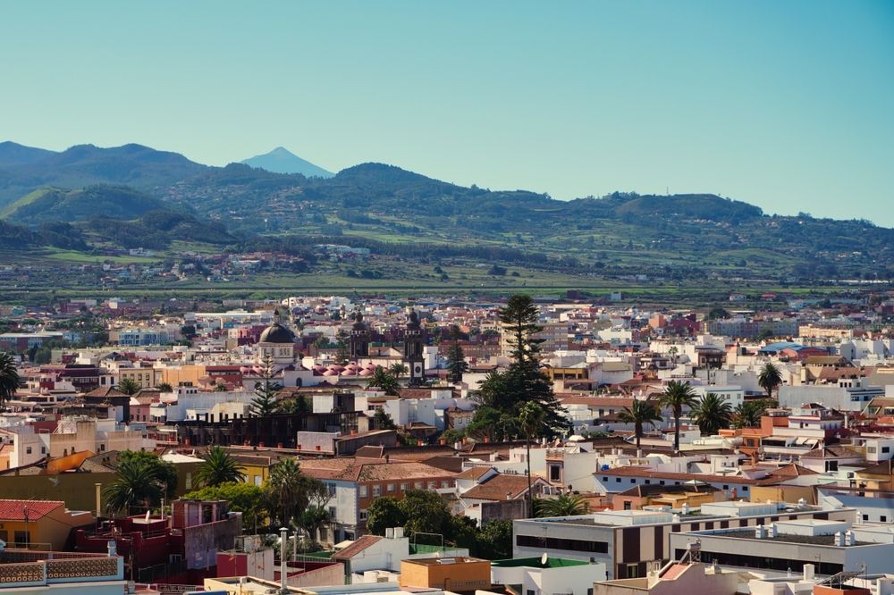 Cityscape with colorful buildings, a church, and mountains in the background under a blue sky.