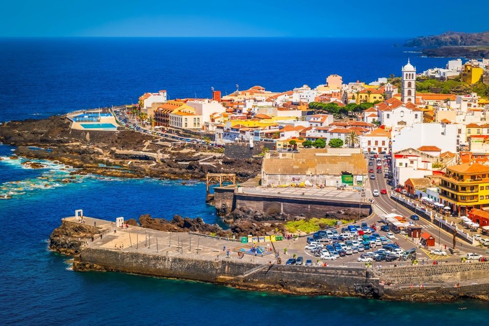 Coastal town with colorful buildings, harbor, and blue ocean under a clear sky.