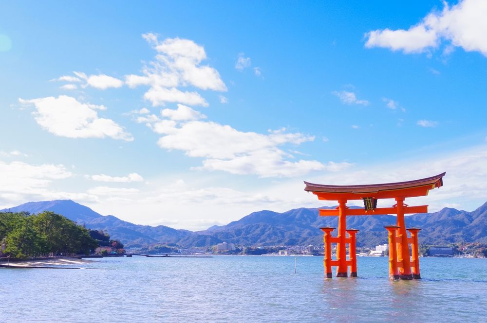Red torii gate in water with mountains and blue sky.