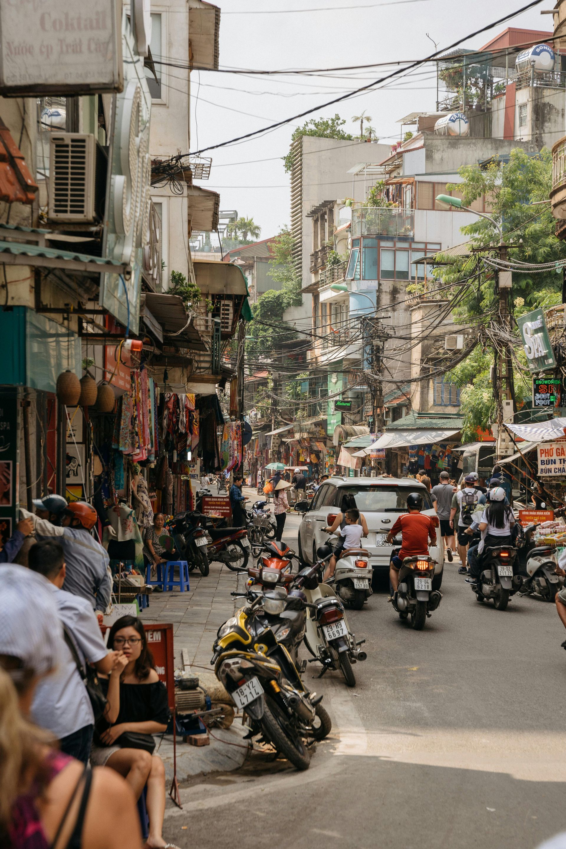 Busy street scene in Hanoi, Vietnam, with motorbikes, pedestrians, and shops.