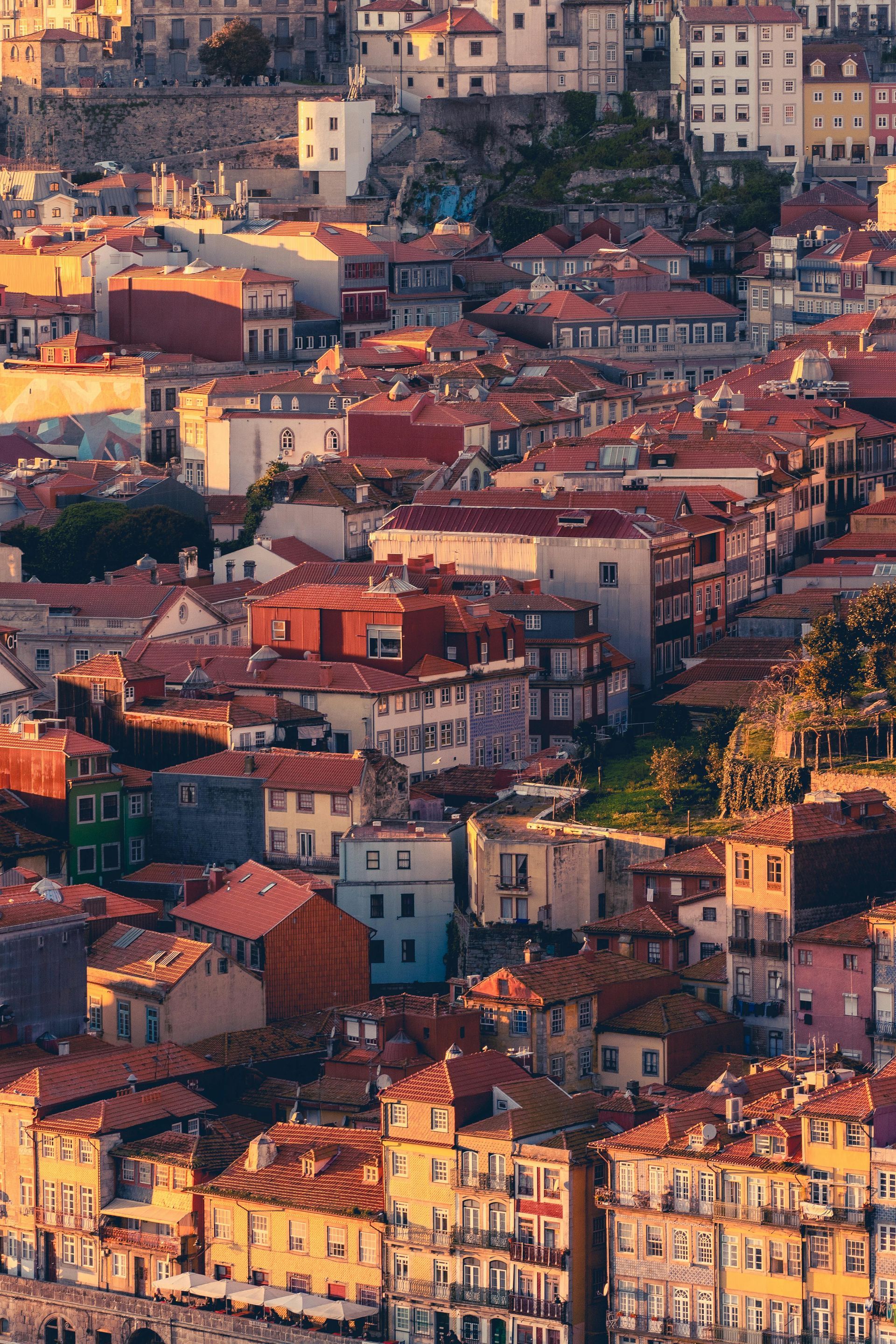 Cityscape of Porto, Portugal, with orange-tiled rooftops, buildings in varying colors, and a warm, sunny glow.