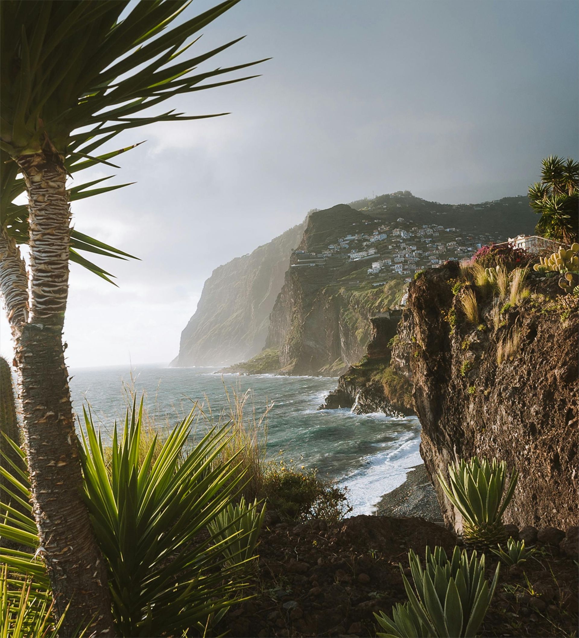 Coastal cliffs with vegetation overlooking a choppy sea under a cloudy sky.