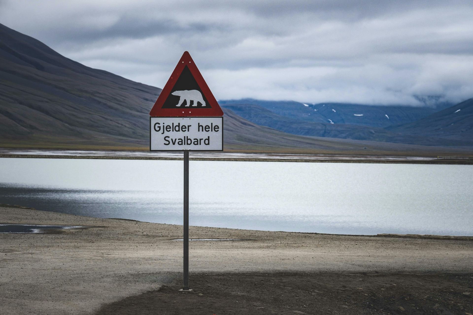 Sign warning of polar bears; mountainous landscape and lake in the background.
