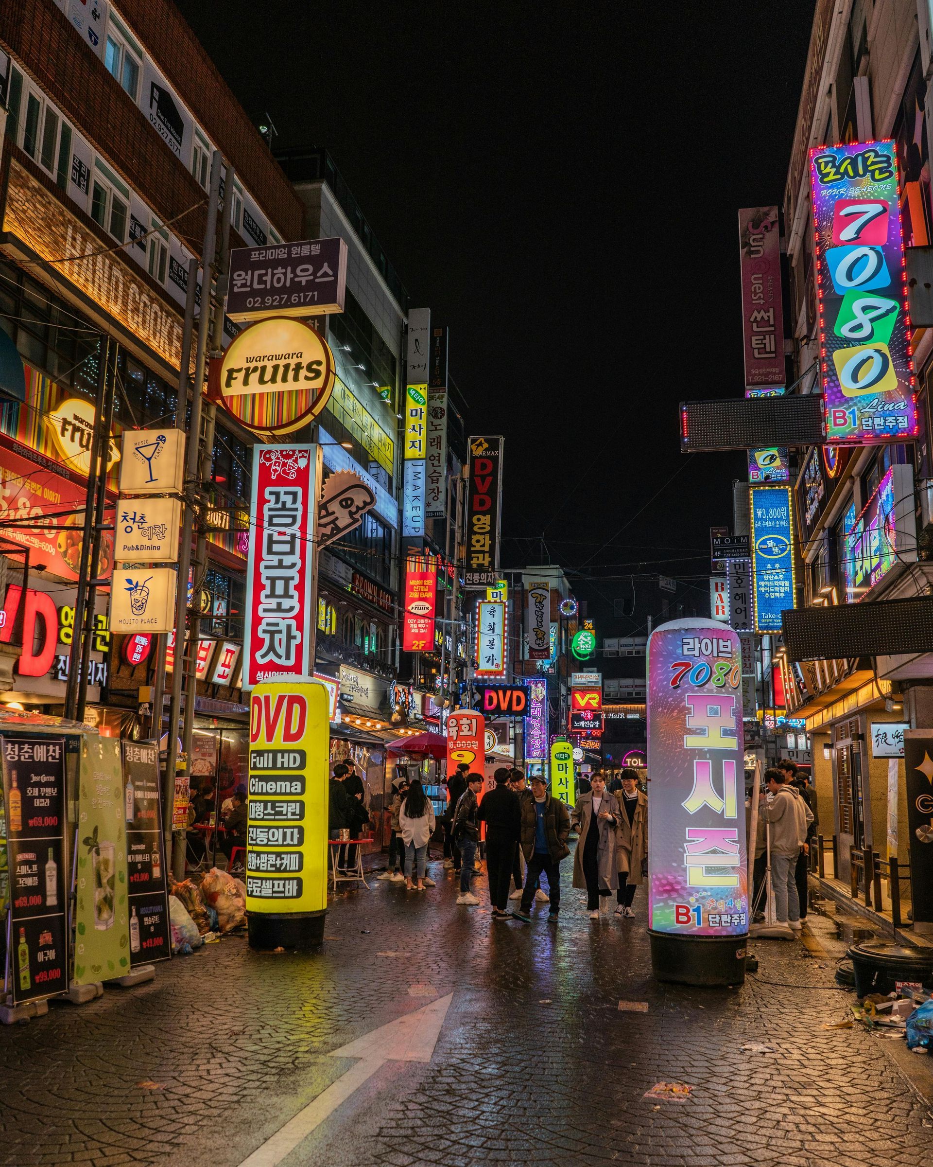 Night scene of a busy street in Korea with vibrant neon signs illuminating buildings and pedestrians.