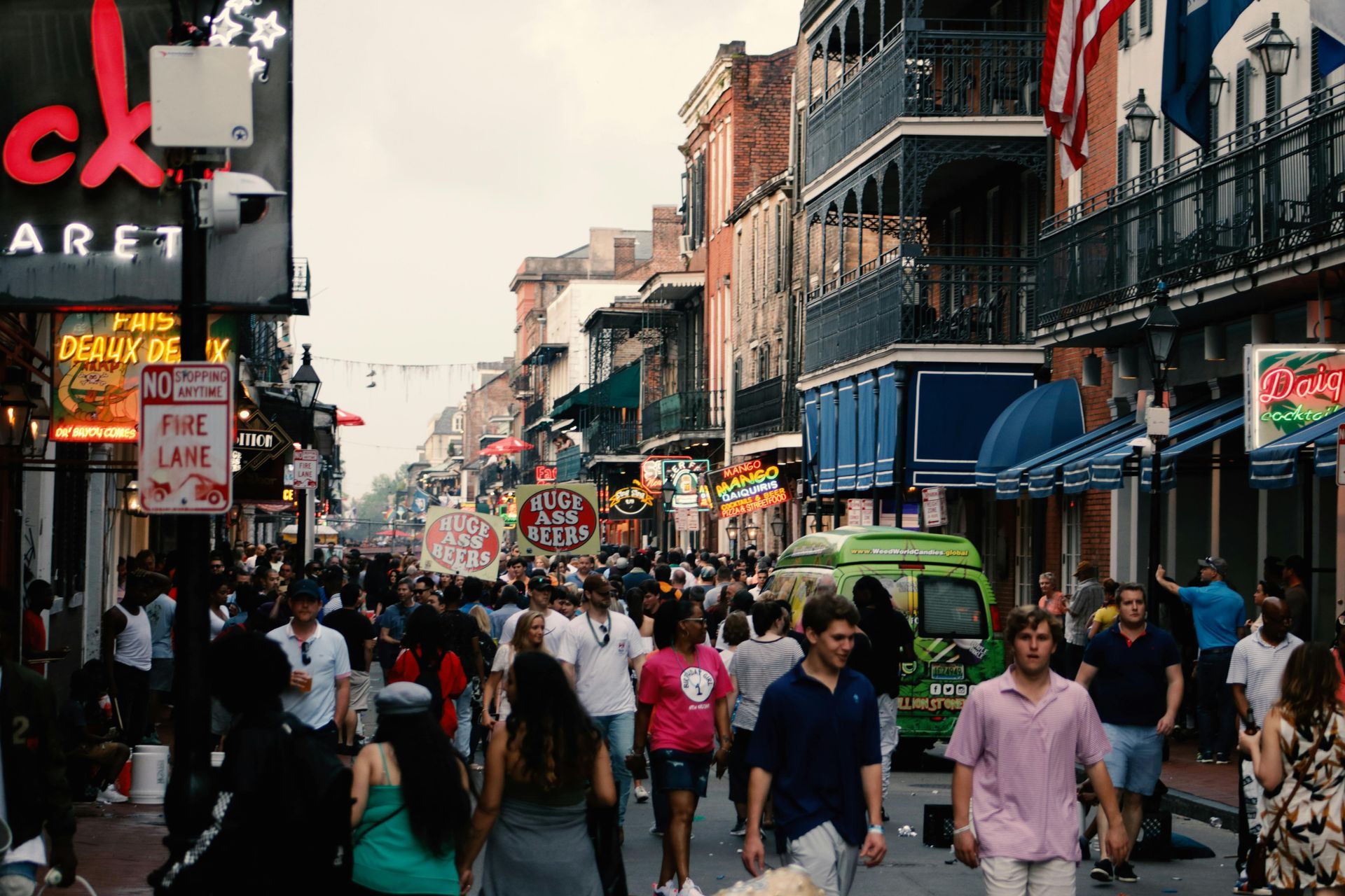 Crowded street in New Orleans; people walking between buildings with balconies and shops, including the