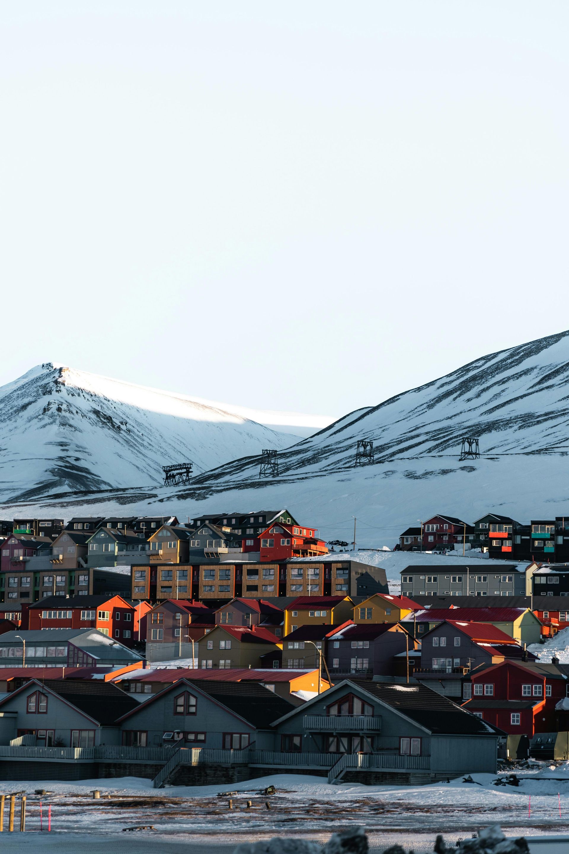 Colorful houses nestled below snow-covered mountains under a bright sky.