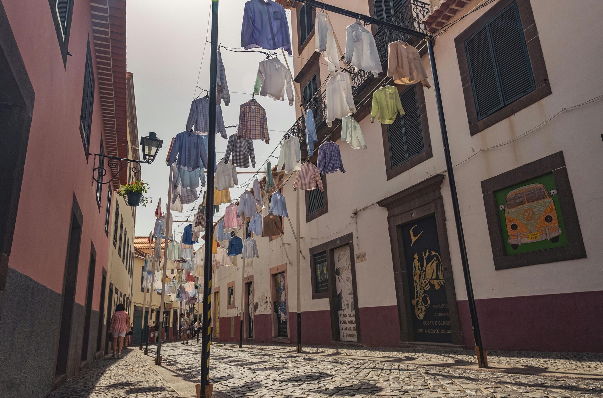 Clothes hanging overhead in a narrow cobblestone street, between buildings with windows and doorways.