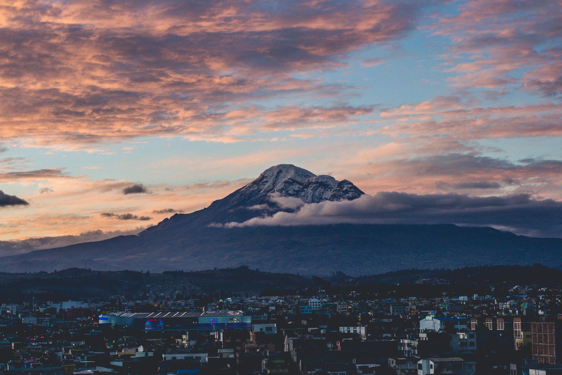 City skyline with mountain backdrop at sunset, pink and blue clouds.