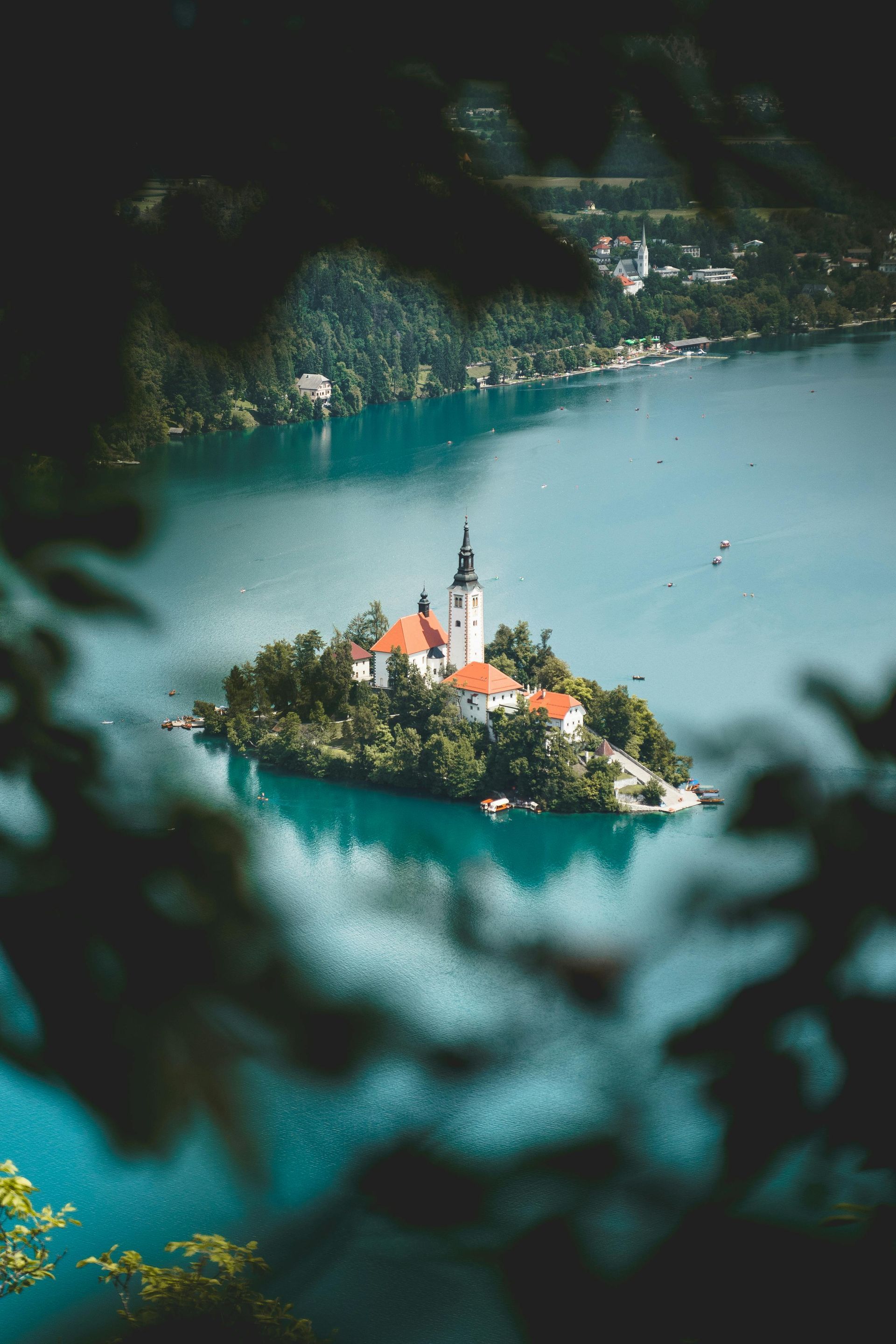 Island church in turquoise lake, surrounded by green foliage. White building with red roof, bell tower.