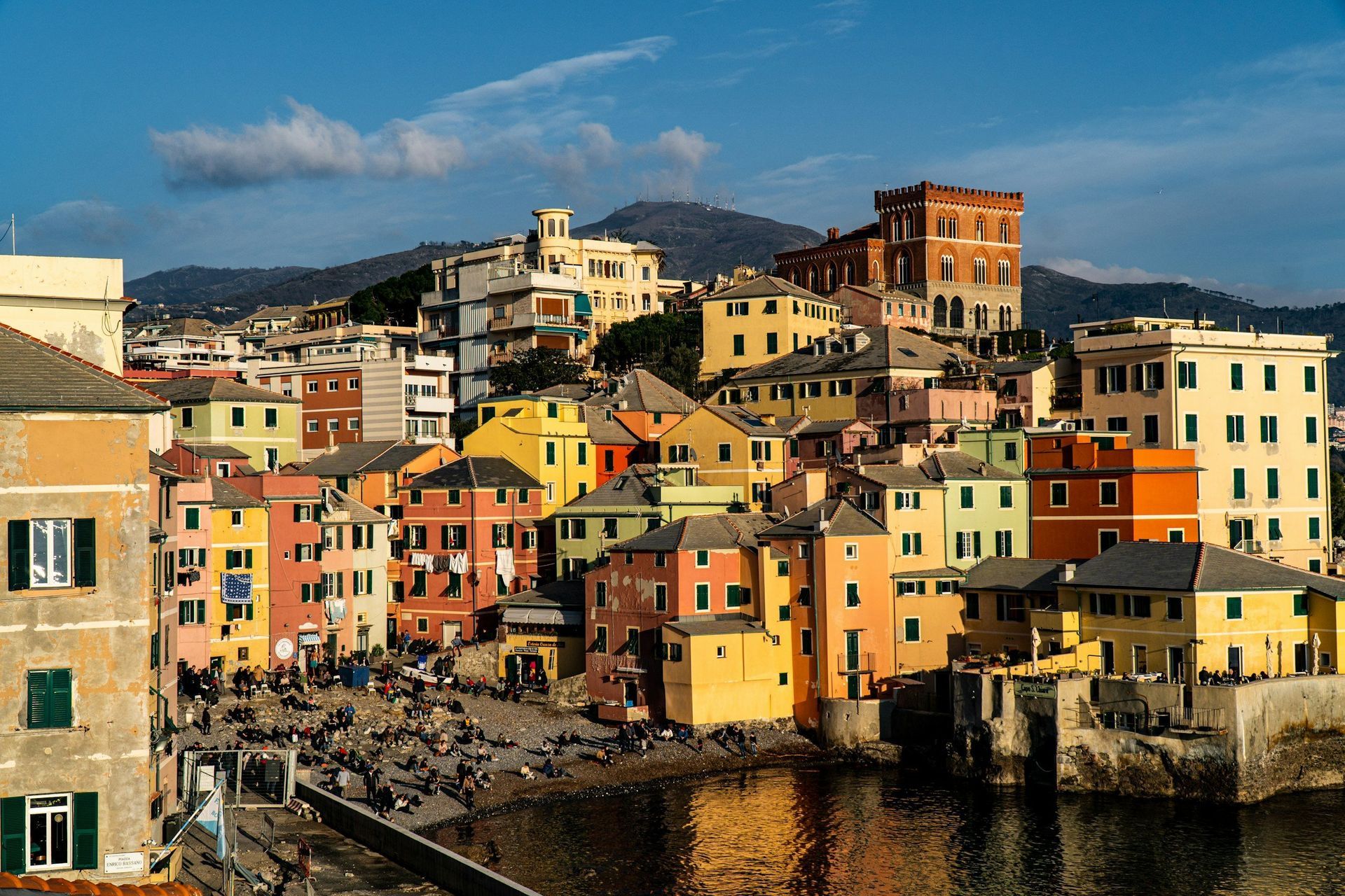 Colorful buildings clustered on a hillside overlooking the water. Sunny day with clear blue sky.