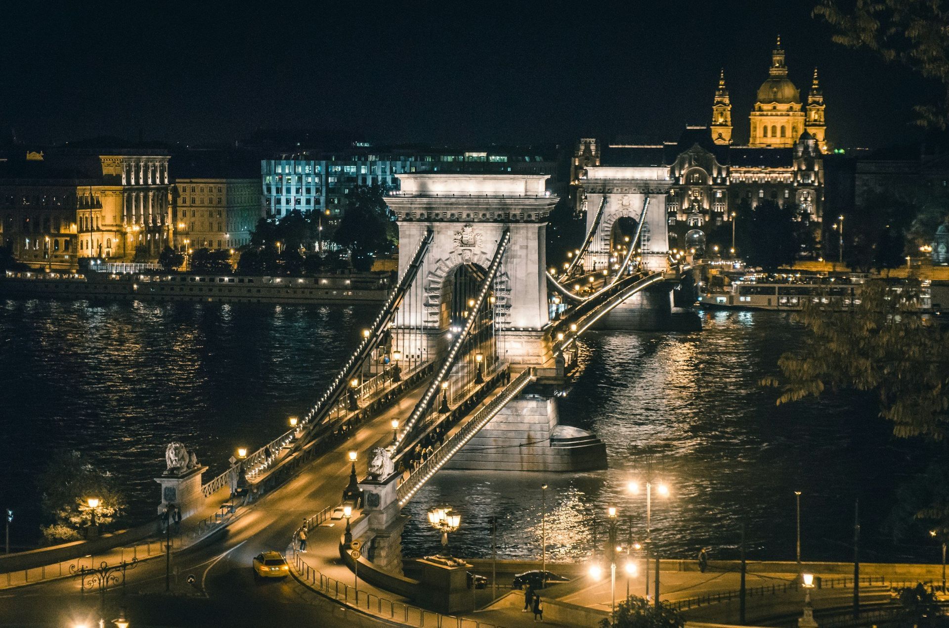 Chain Bridge at night, Budapest, Hungary. Lit suspension bridge over river, buildings in background.