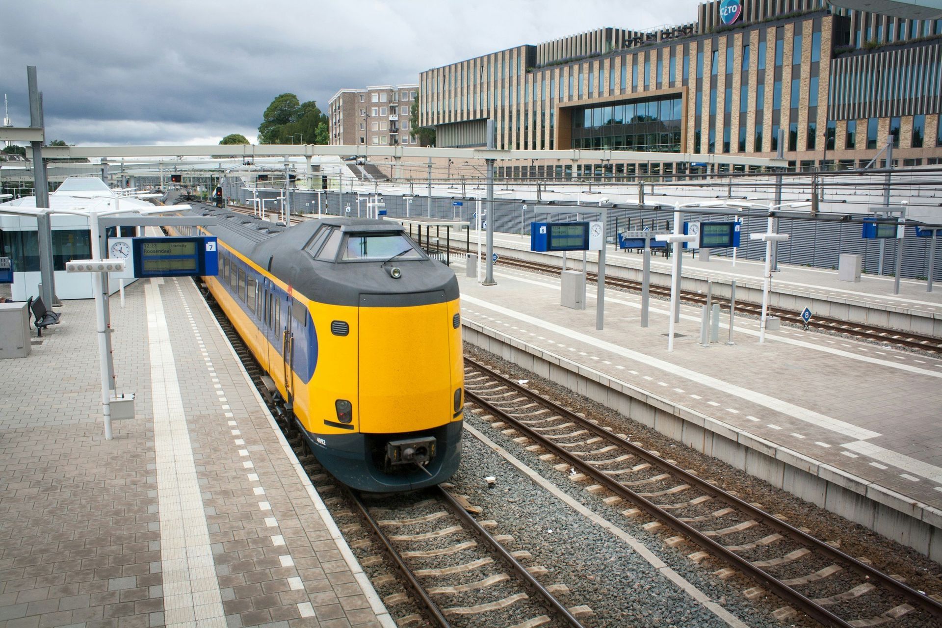 Yellow and blue train at a station with modern architecture on a cloudy day.
