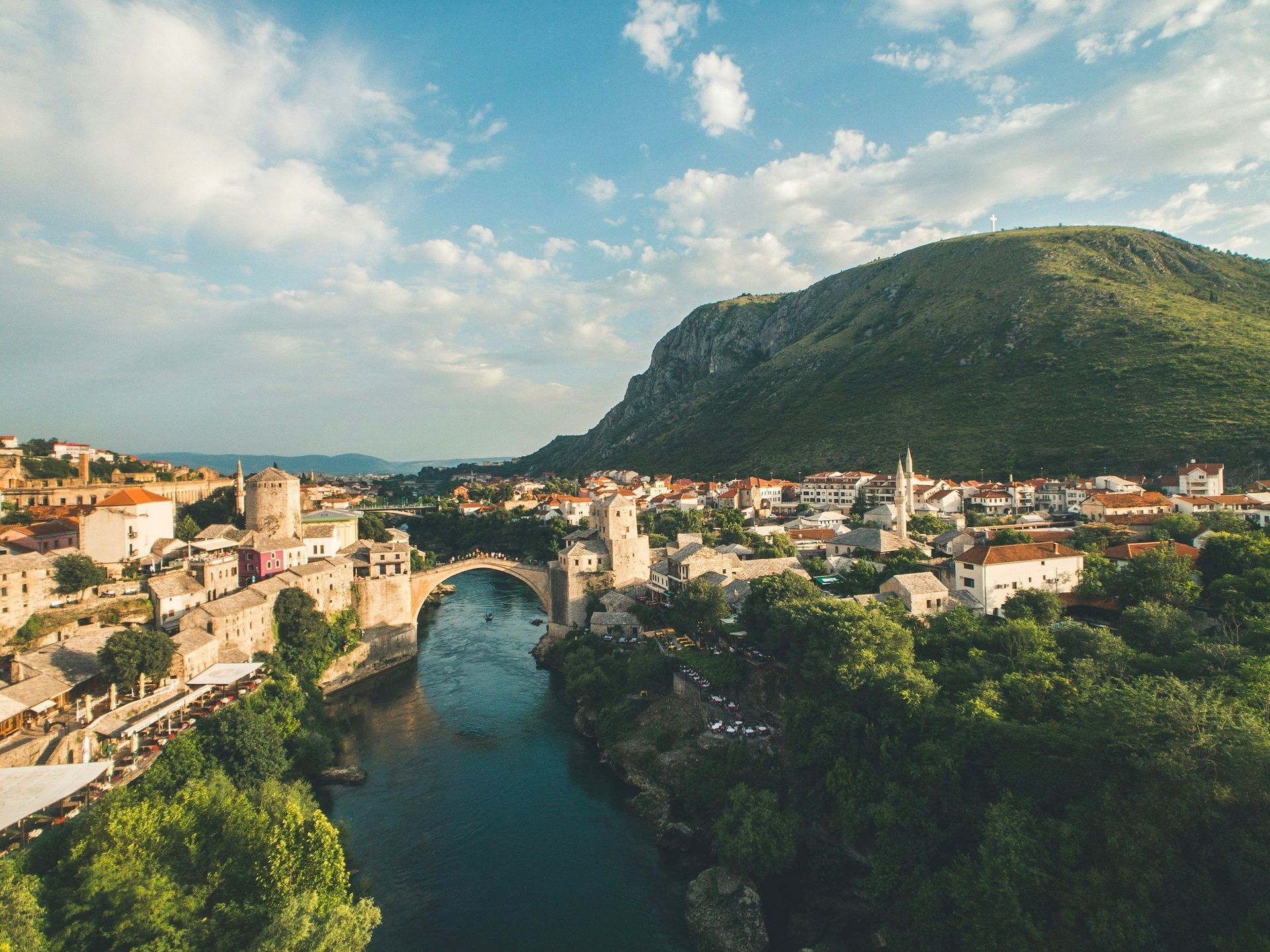 Mostar, Bosnia and Herzegovina, with the iconic Stari Most bridge over a river, and a mountain in the background.