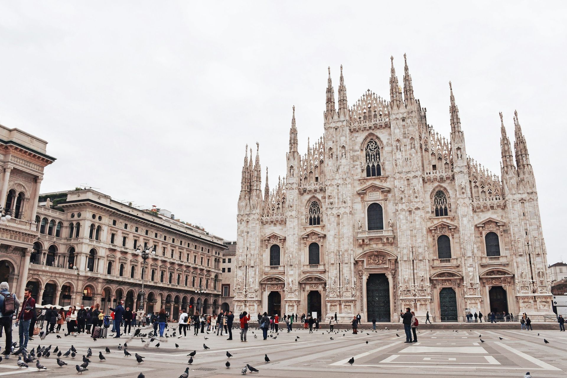 Milan Cathedral facade and plaza with people and pigeons.