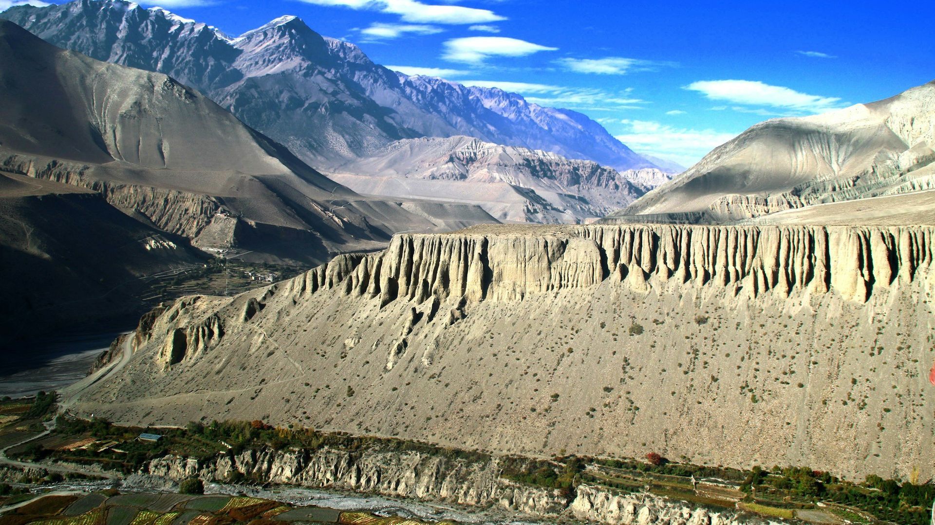 Mountainous landscape with valley and canyon walls under a blue sky.