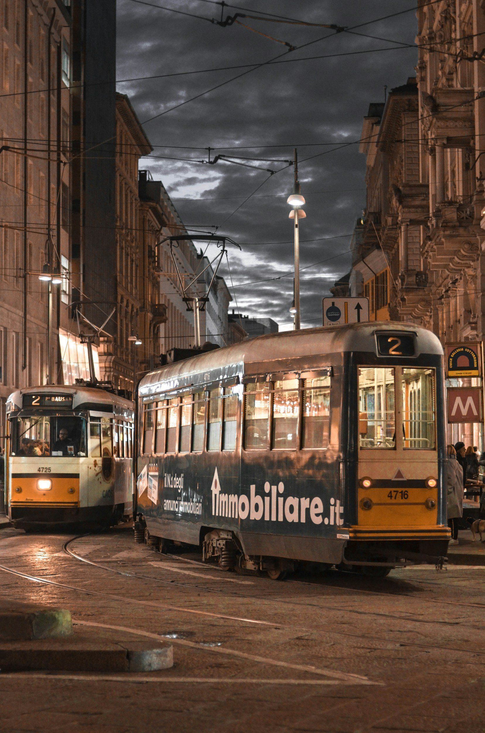 Two trams on wet cobblestone street at night, flanked by buildings.