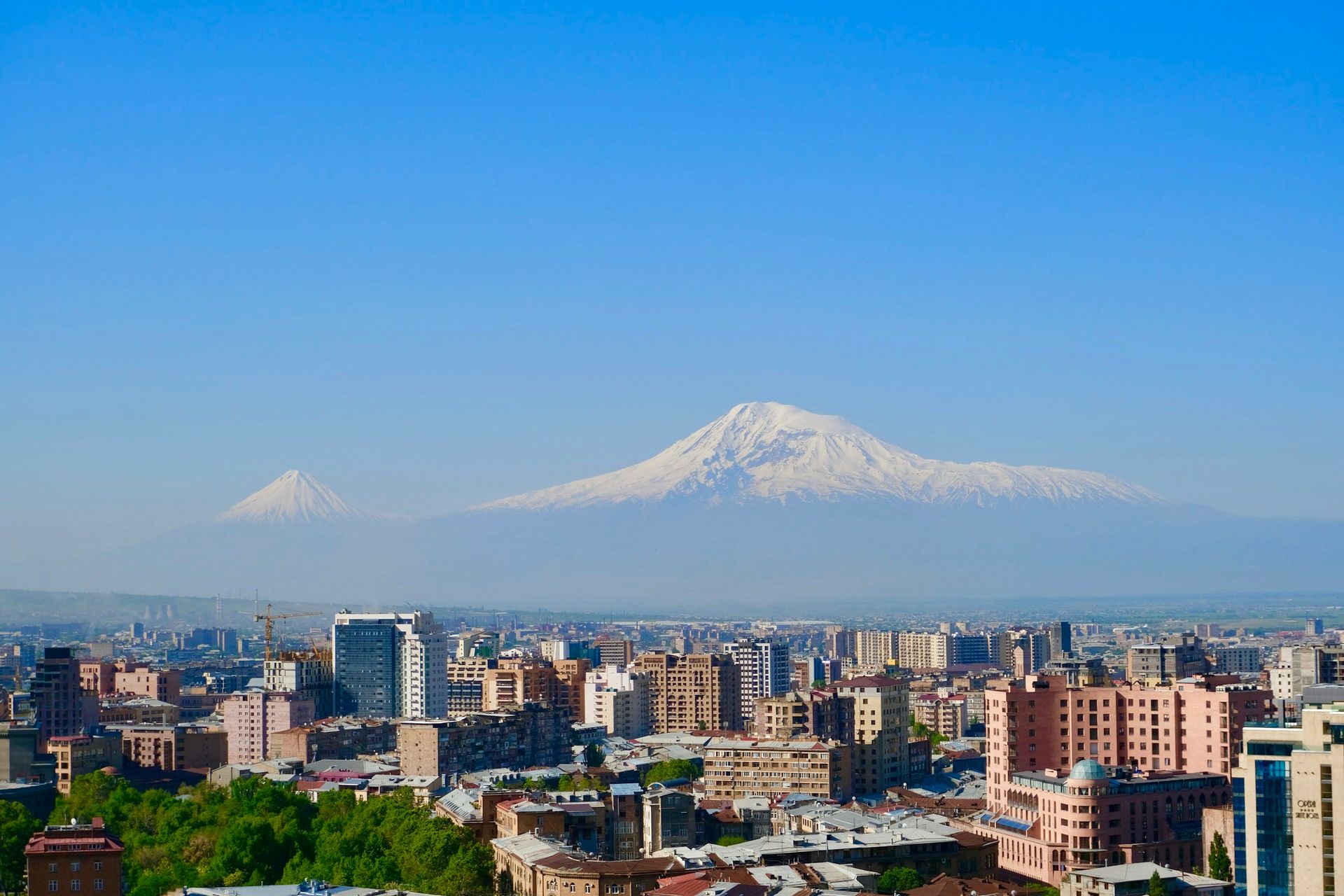 Cityscape with snow-capped Mount Ararat in the background, under a clear blue sky.