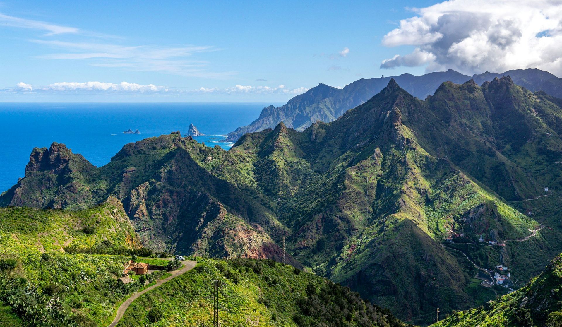 Mountainous green terrain meets the blue ocean under a bright, clear sky.