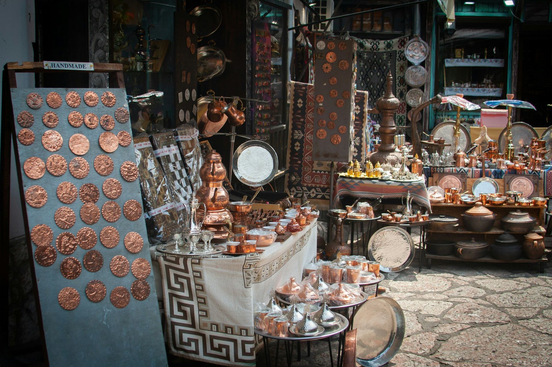 Copperware shop in an outdoor market displaying plates, pots, and other handcrafted items.