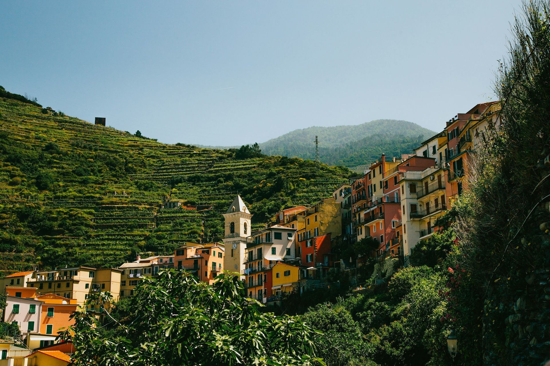 Colorful buildings cascade down a hillside in an Italian village, with a church steeple and terraced gardens.