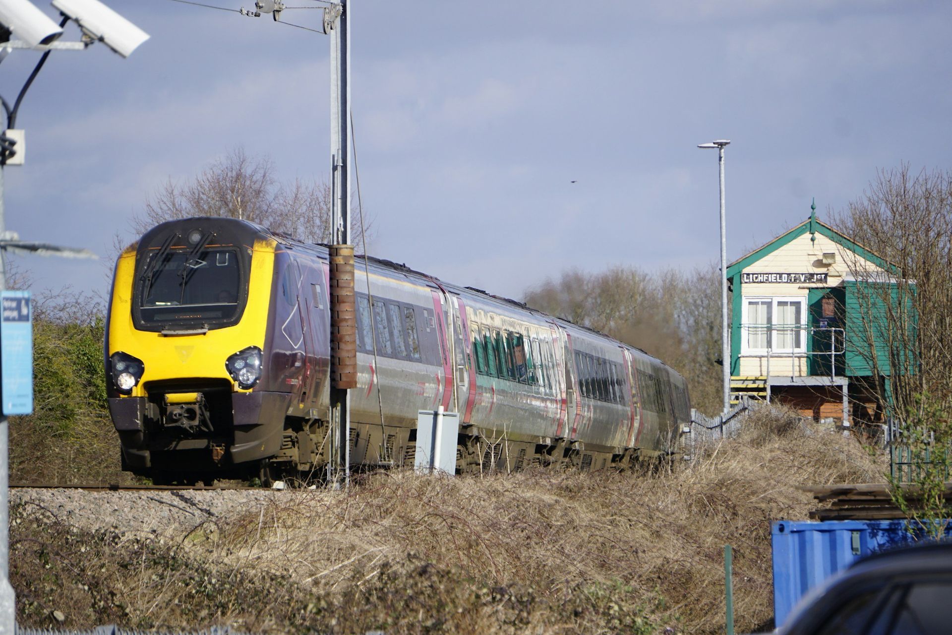Train passing a signal box on tracks, with a yellow and purple front.
