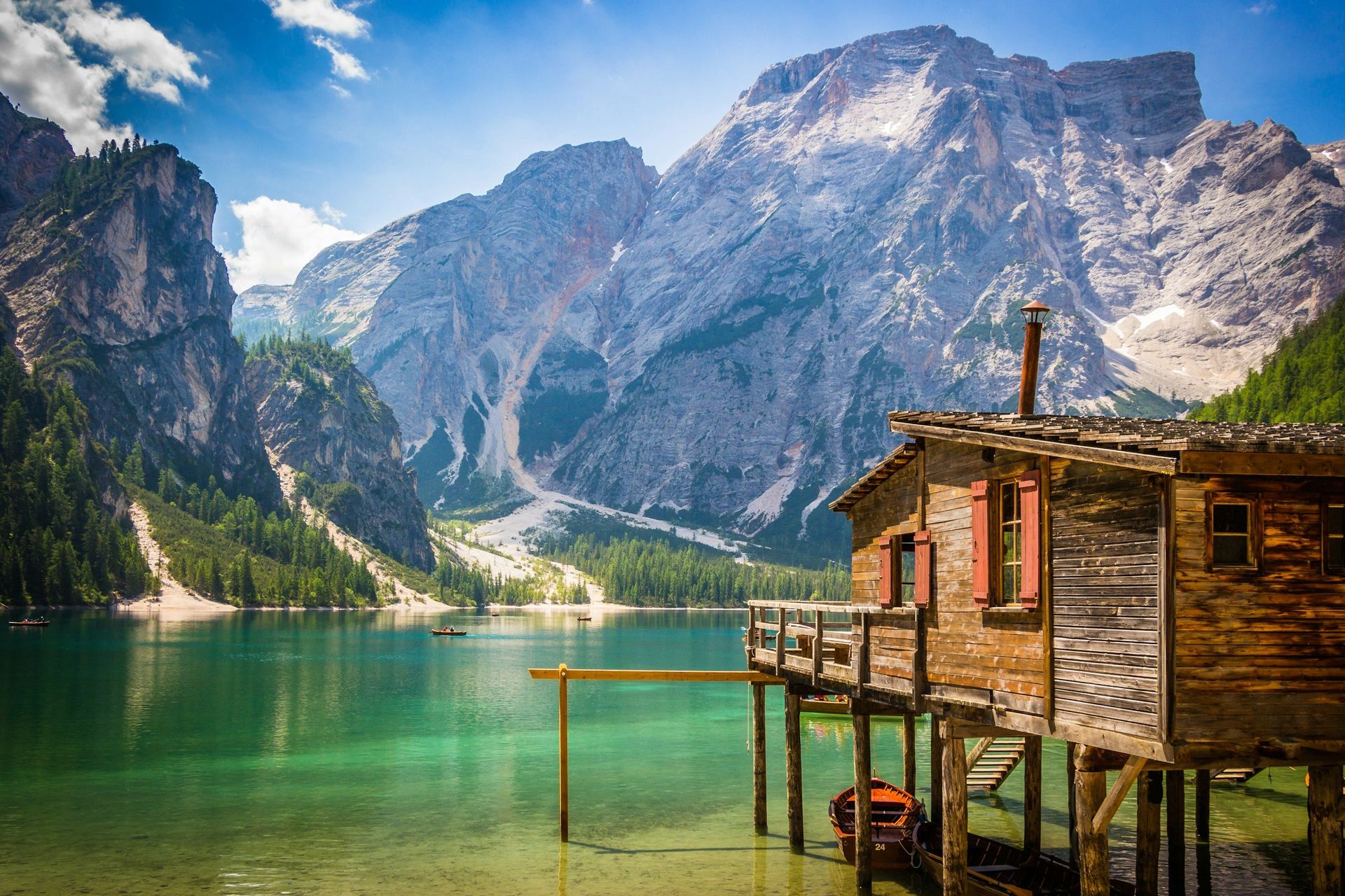 Wooden cabin on stilts over turquoise lake, mountains in background.