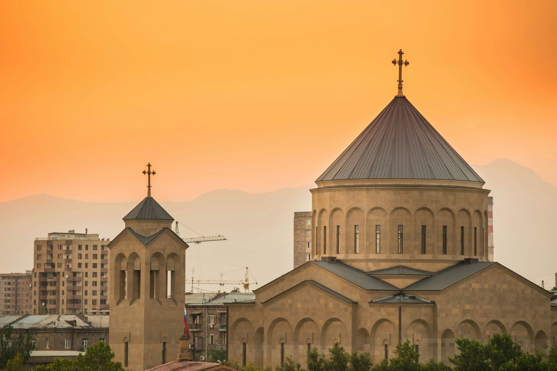 Church with cross on top, against an orange sunset; Yerevan, Armenia.