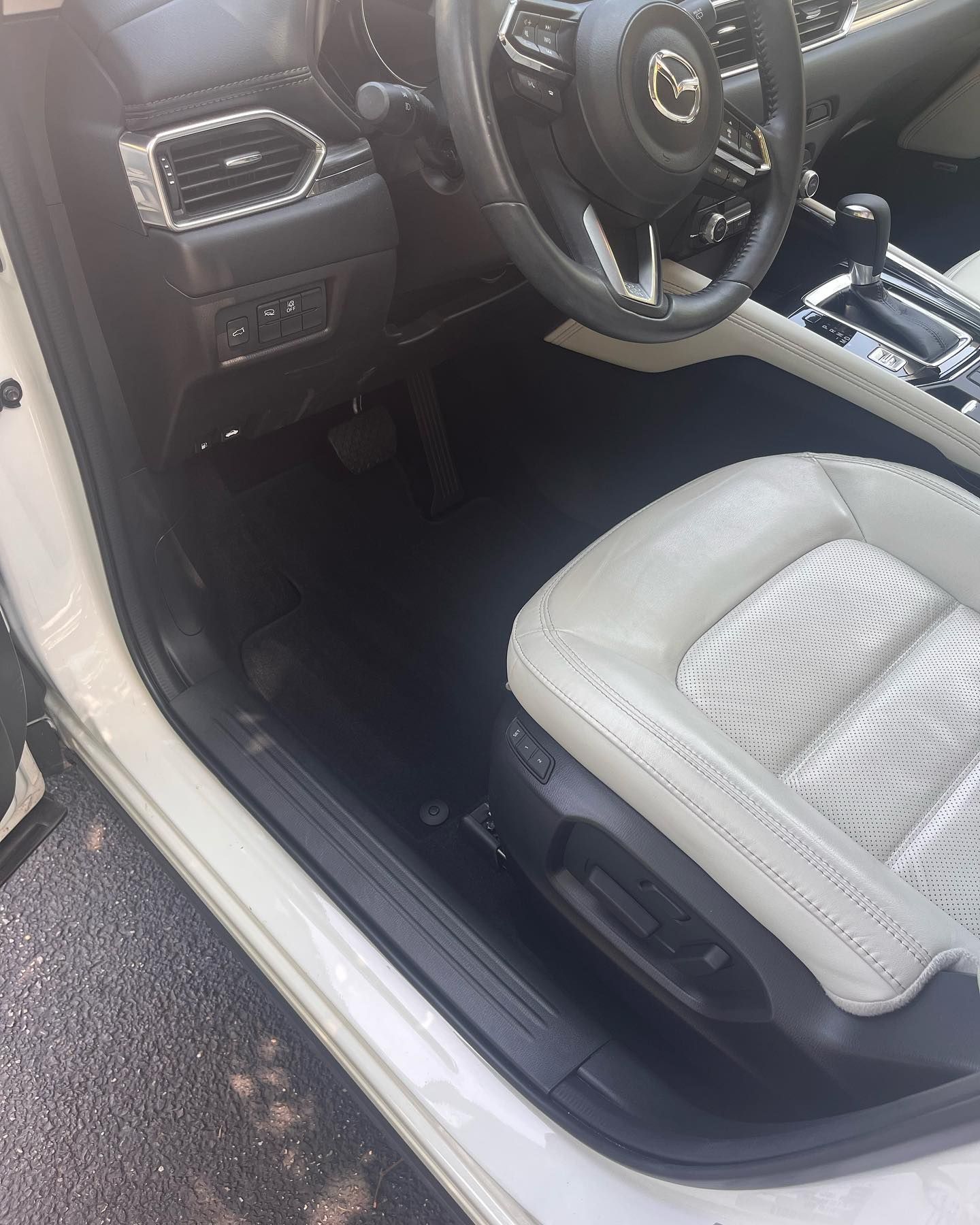 Interior car view with a white leather seat, black floor mats, and steering wheel.
