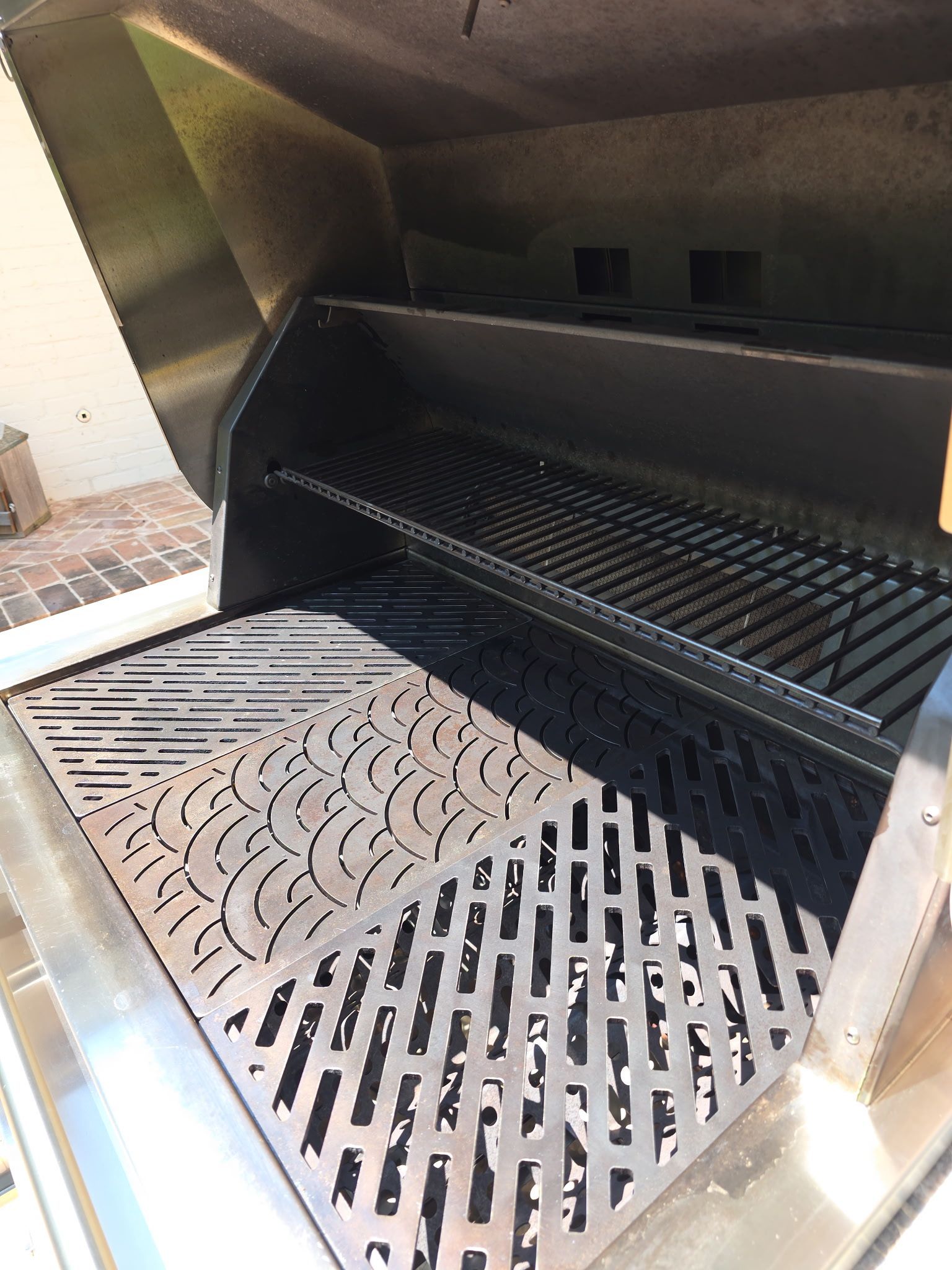 Open stainless steel grill interior with black grates and decorative metal bottom plate.