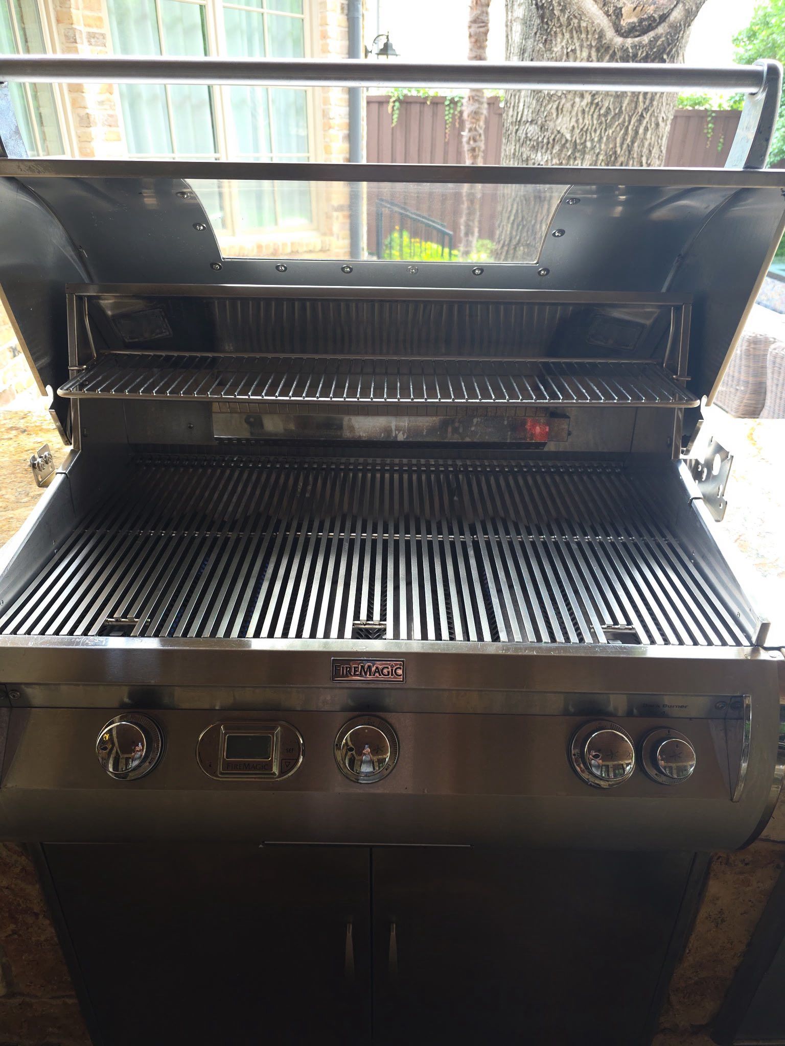 Stainless steel outdoor grill with open lid, knobs, and grill grates.