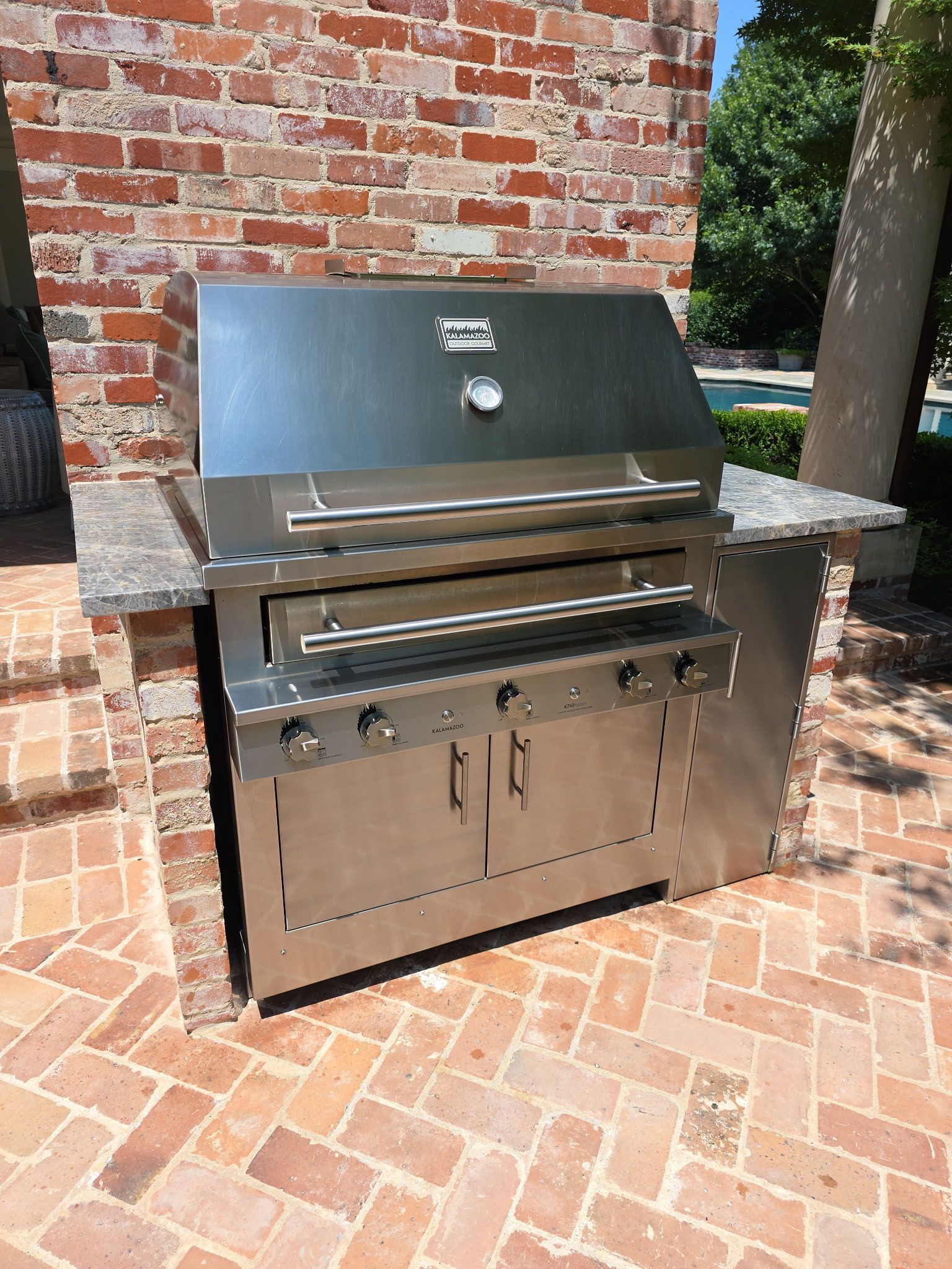 Stainless steel outdoor grill built into a brick and granite structure.