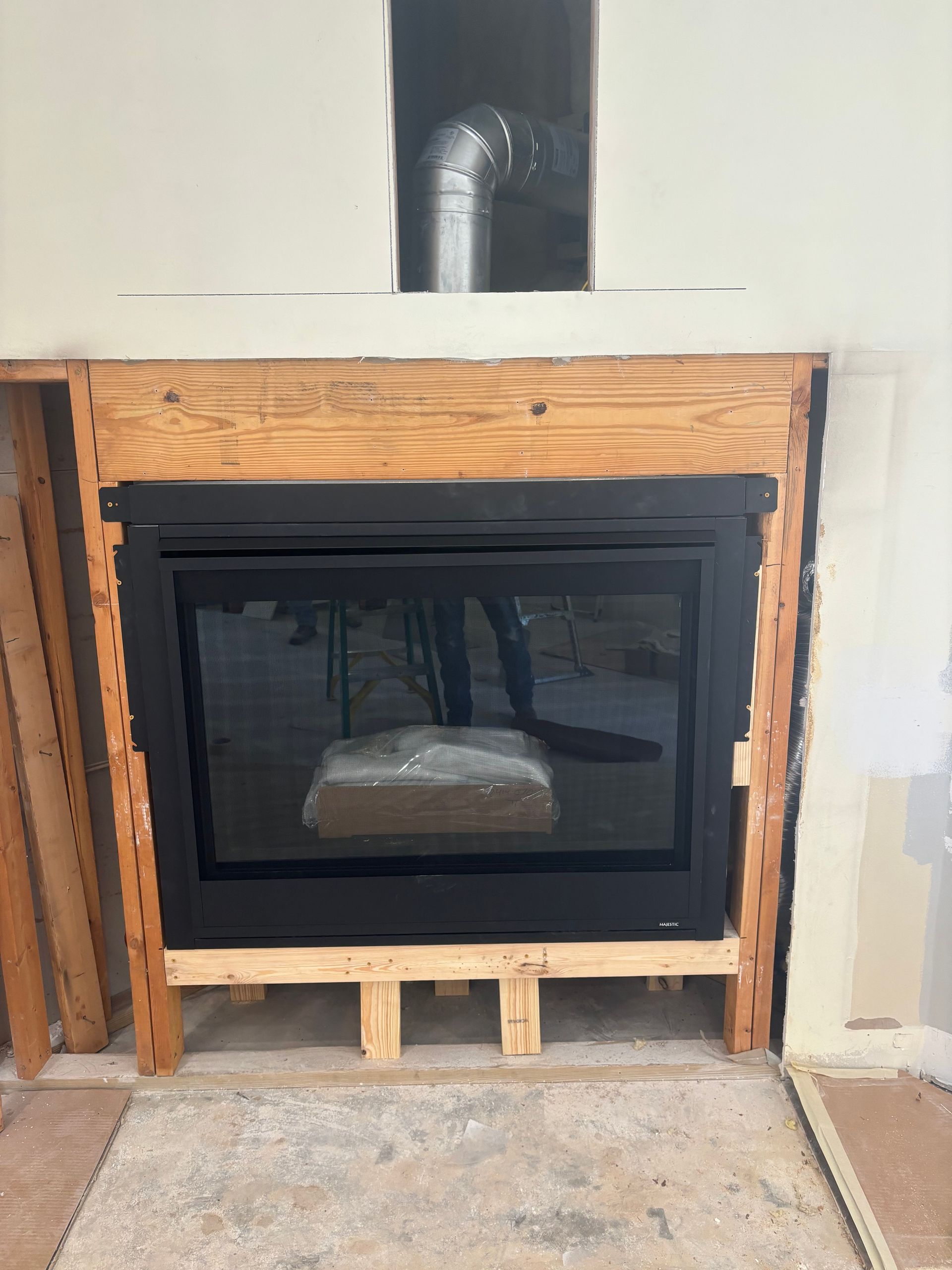 Fireplace insert installed in a wooden frame, set against a wall with a visible vent pipe.