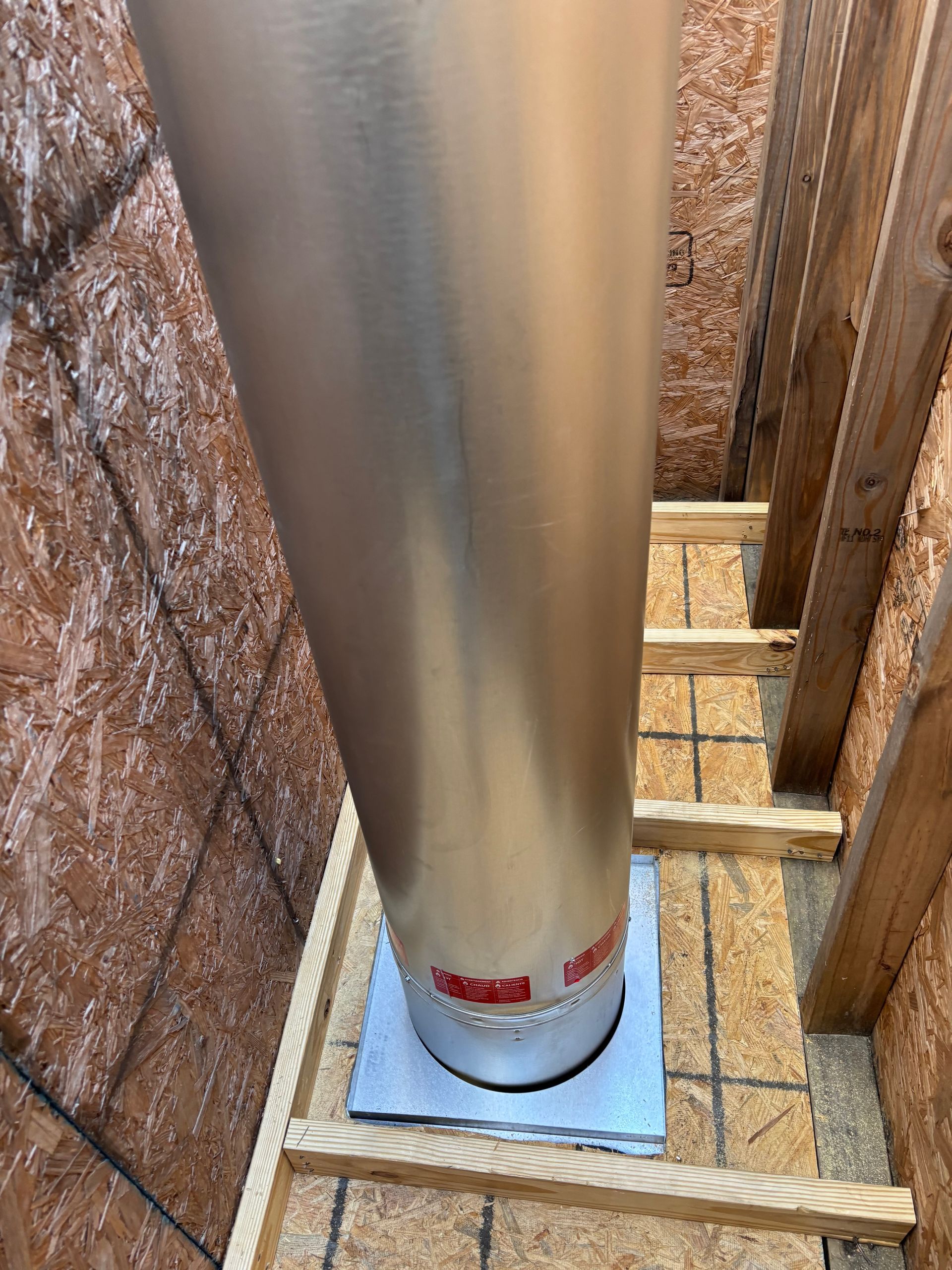 Silver exhaust pipe in a wood-framed attic space, resting on a wooden base.