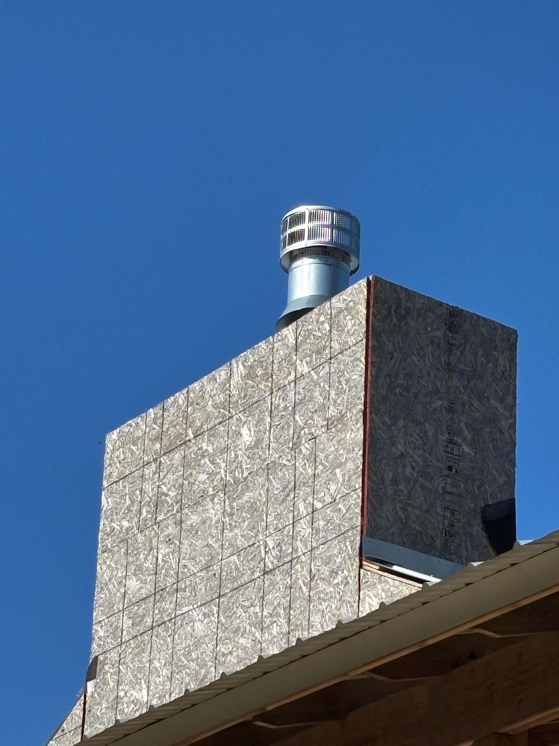 Chimney with metal cap against a clear blue sky. The chimney is covered with textured panels.