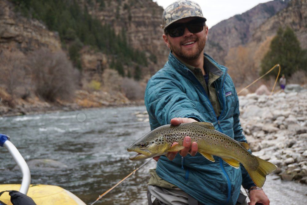 A man is holding a brown trout in front of a river.