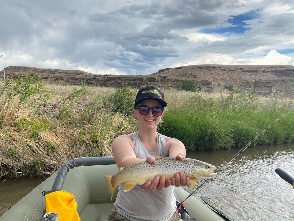 A woman is sitting in a boat holding a brown trout.