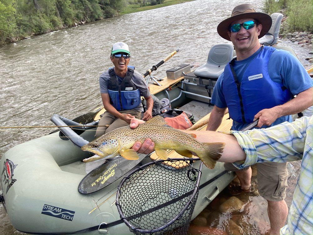 Two men are standing next to a boat holding a large fish.