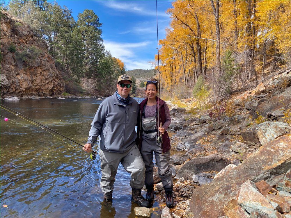 A man and a woman are standing in a river holding fishing rods.