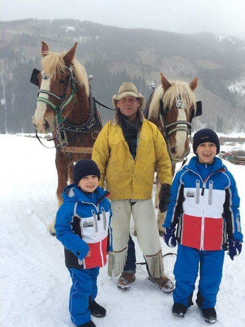 A man and two children standing in front of two horses in the snow