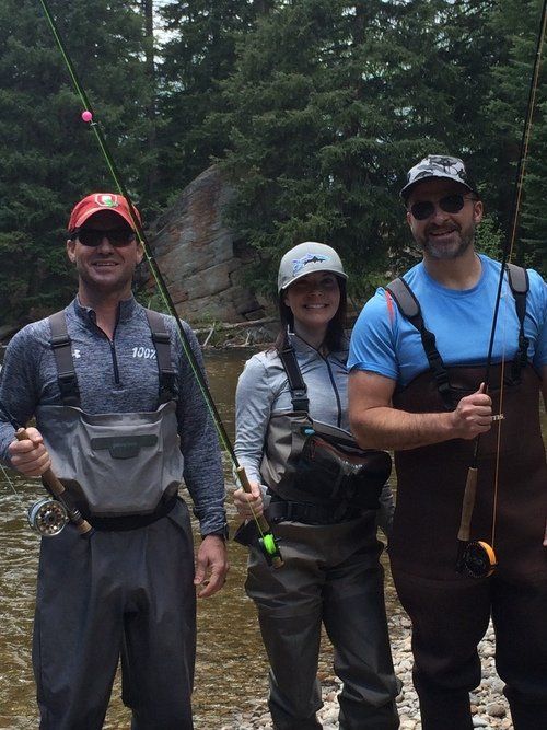 Three people are standing next to each other holding fishing rods.